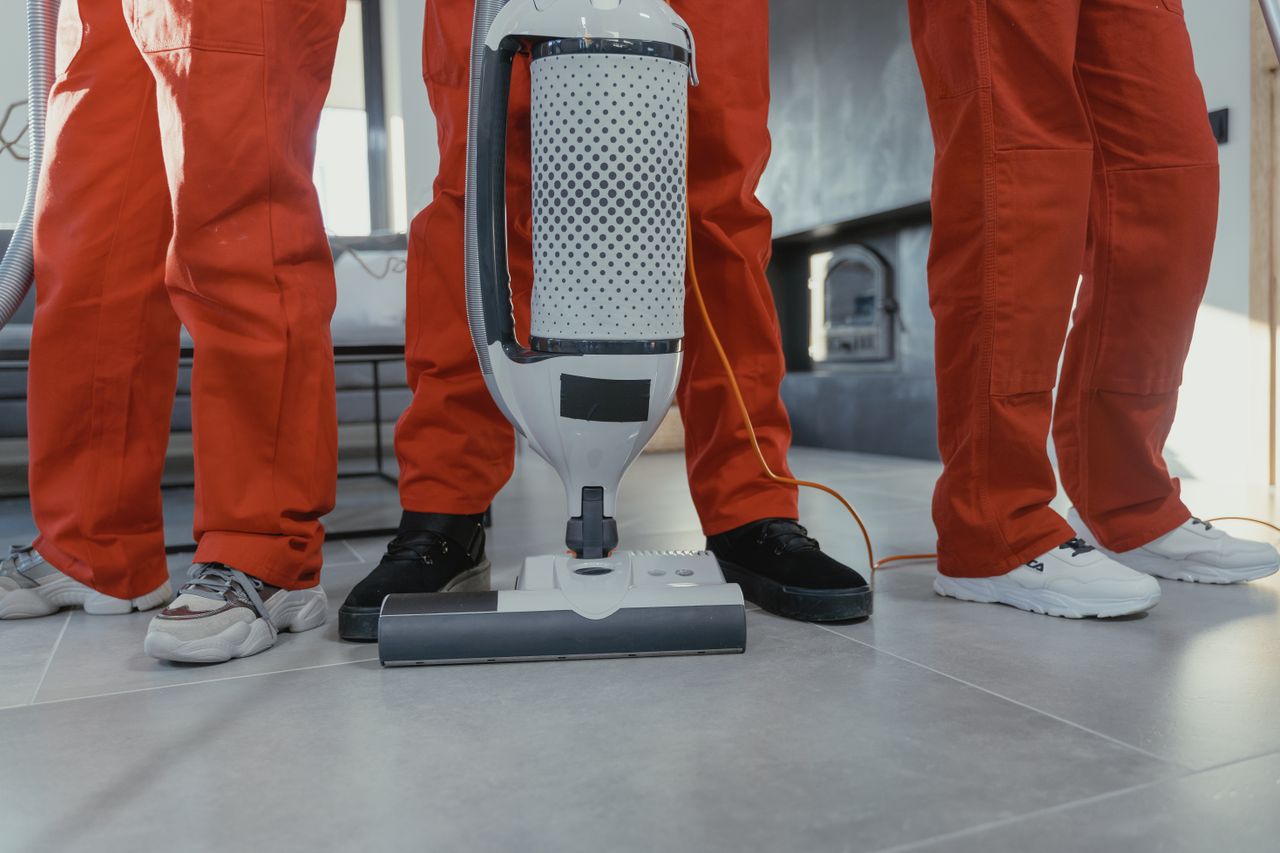 Une équipe de nettoyeurs professionnels en uniformes rouges utilisant un aspirateur à l’intérieur.
